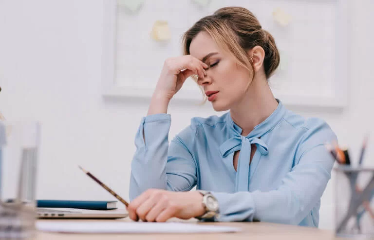 Stress: mulher com a mão no rosto demonstrando estar estressada em ambiente de trabalho
