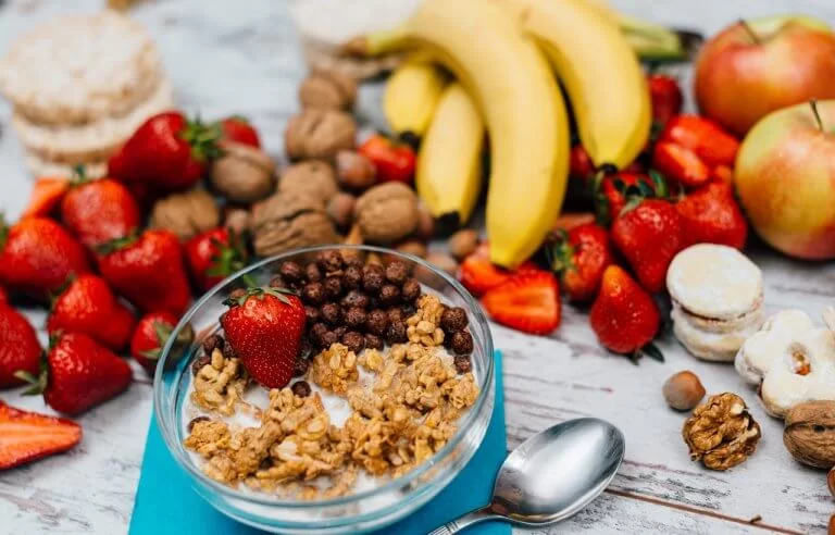 Mesa com várias frutas, cereais como nozes, doces como macarrons e pão de arroz ao fundo