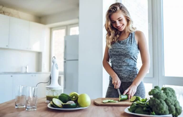 Mulher feliz cortando legumes, frutas e verduras para suco verde: alimentação saudável