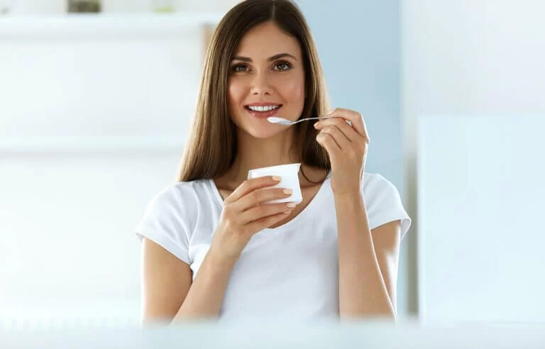 Mulher de branco sorrindo enquanto toma iogurte natural simbolizando vida saudável e leve