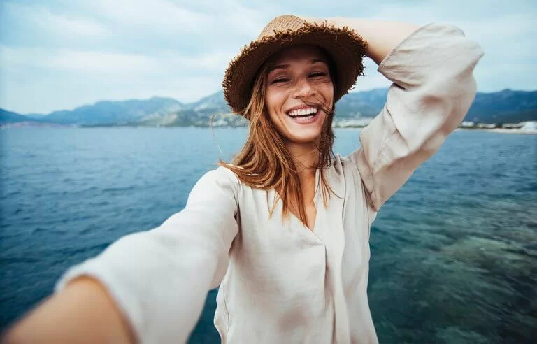Mulher feliz com mar ao fundo tirando selfie em passeio marítimo: vivendo a vida feliz