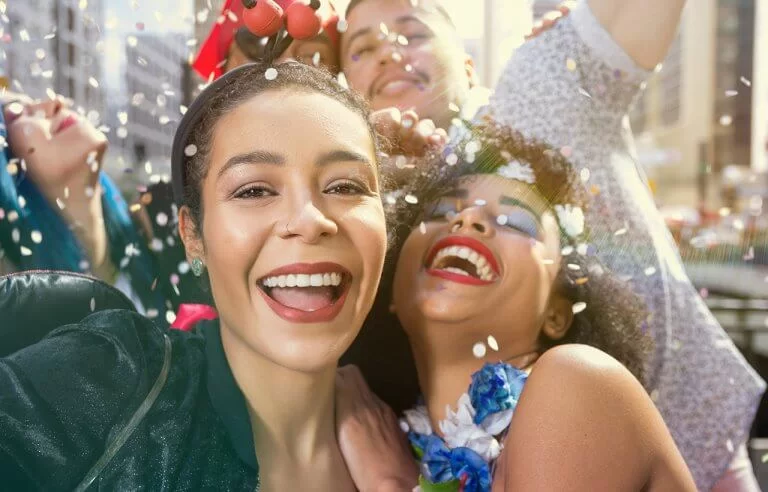 Jovens se divertindo no carnaval com cofetes caindo e eles posam felizes para foto