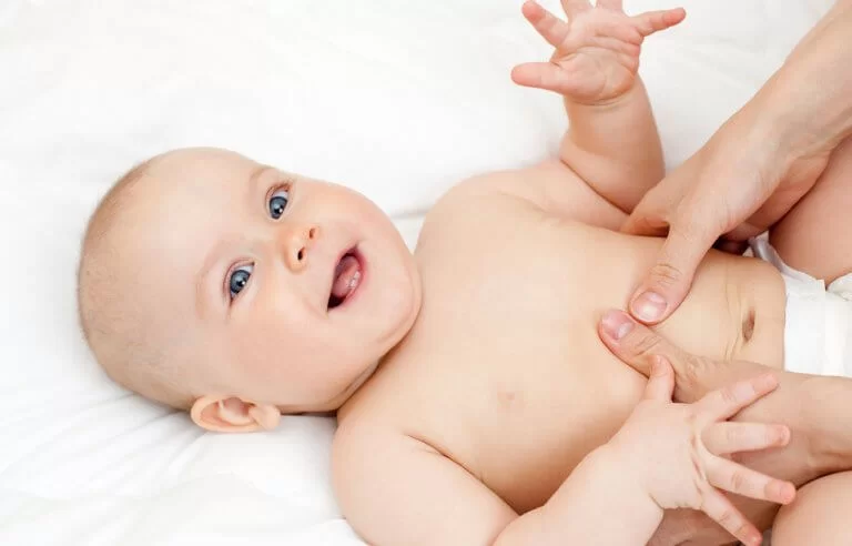 Bebê sorrindo enquanto alguém pressiona sua barriga: massagem para intestino preso