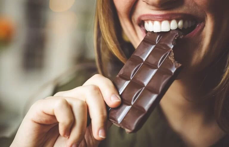 Mulher comendo barra de chocolate com um belo sorriso no rosto