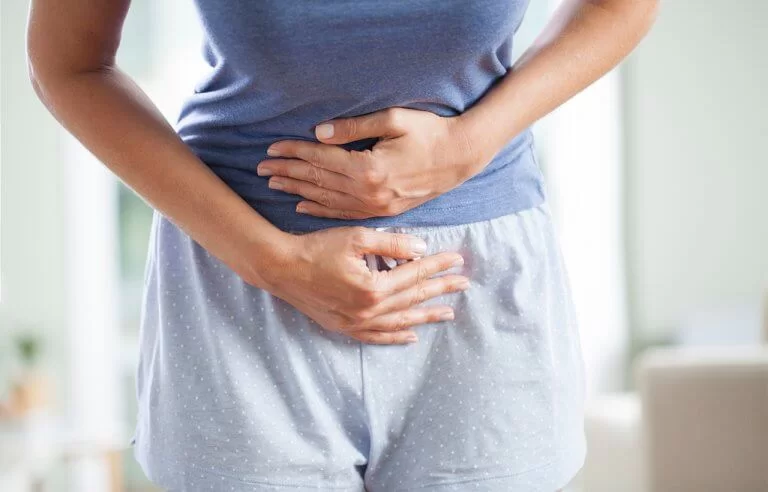 Mulher com as mãos em cima da barriga e corpo meio inclinado para frente demonstrando dor