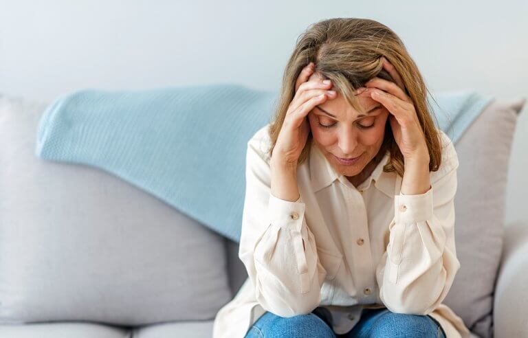 Mulher com mãos nas temporas sentada em sofá mostrando estar com dor de cabeça