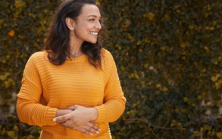Mulher sorrindo com as mãos na barriga refletindo seu bom humor por ter intestino saudável