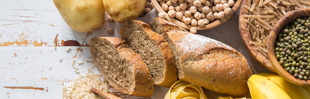 Imagem de um pão cortado e outros alimentos simbolizando carboidratos