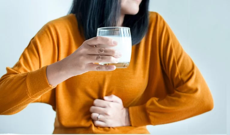 Indigestão: mulher com as mão na barriga apertando-a e com um copo de leite na outra mão
