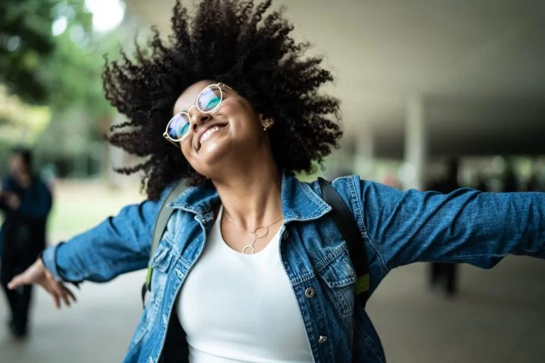 Mulher negra de óculos com sorriso e braços abertos: felicidade e alegria de viver