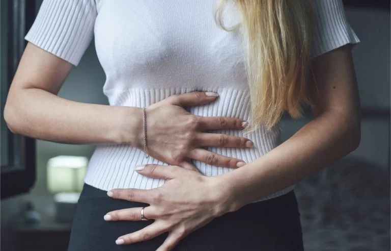 Mulher loira com as 2 mãos em toda a região da barriga