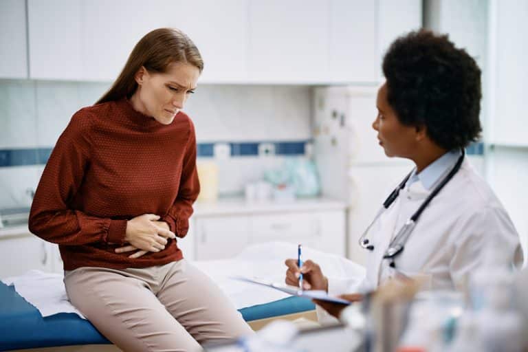 Mulher de blusa vermelha com dores no abdômen conversando com uma médica